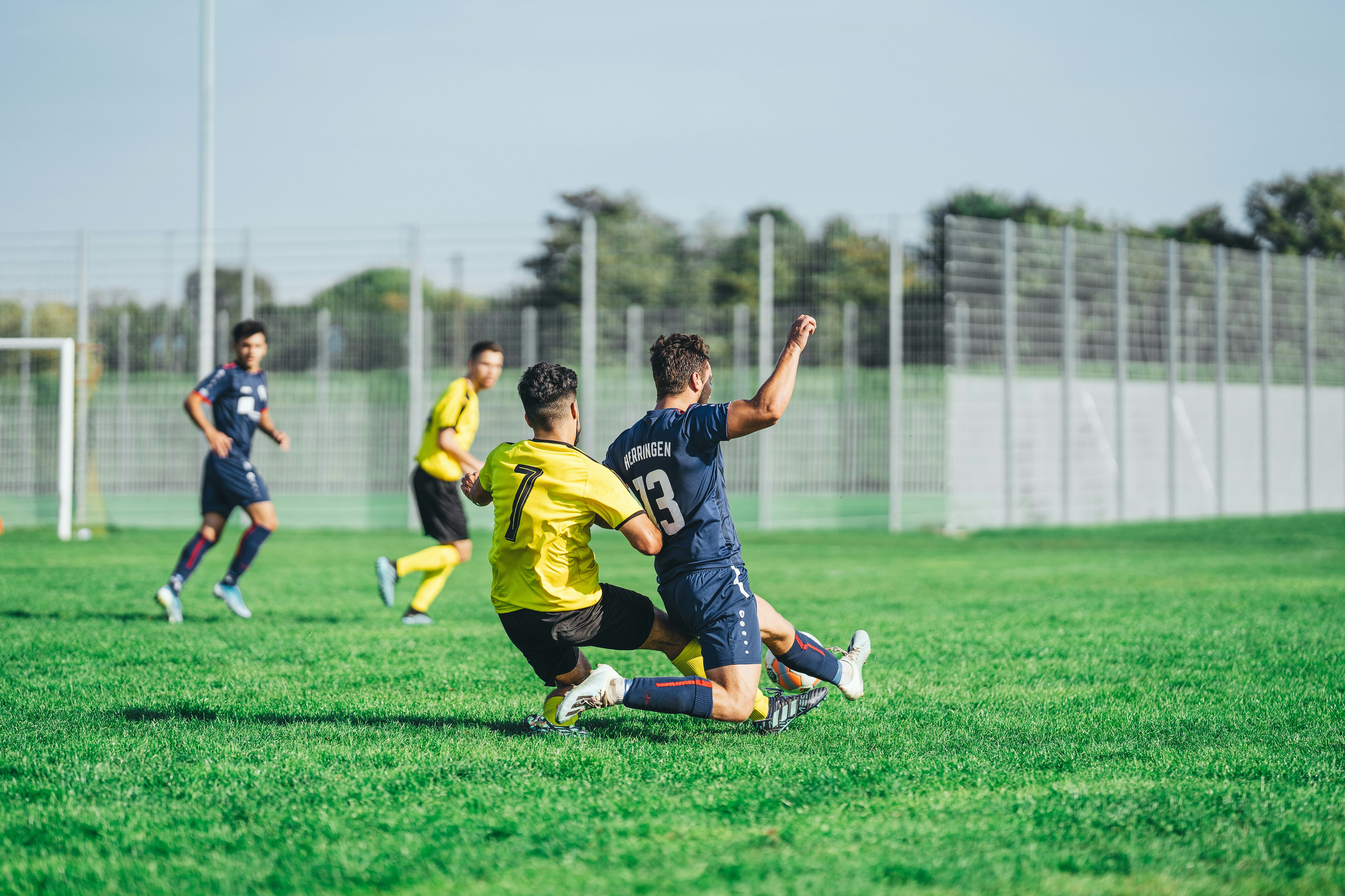 man in yellow and black jersey shirt kicking soccer ball on green grass field during daytime